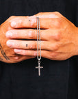 Silver cross necklace held between tattooed hands against a black background