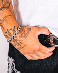 Person with tattoos wearing a bracelet and holding a phone with a white background