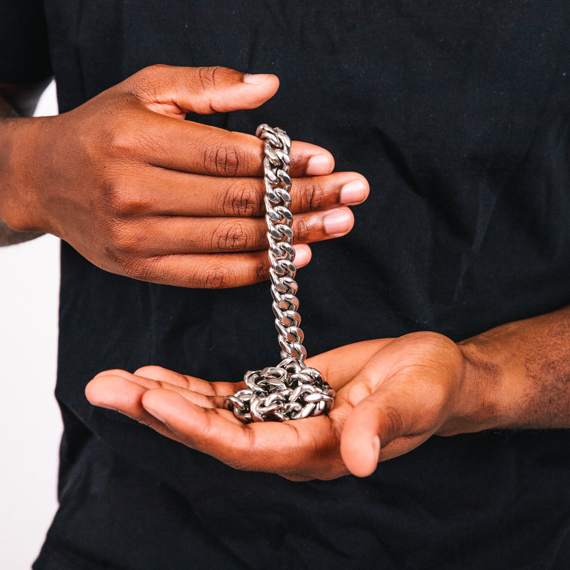 Person holding a silver chain in their hands against a black background