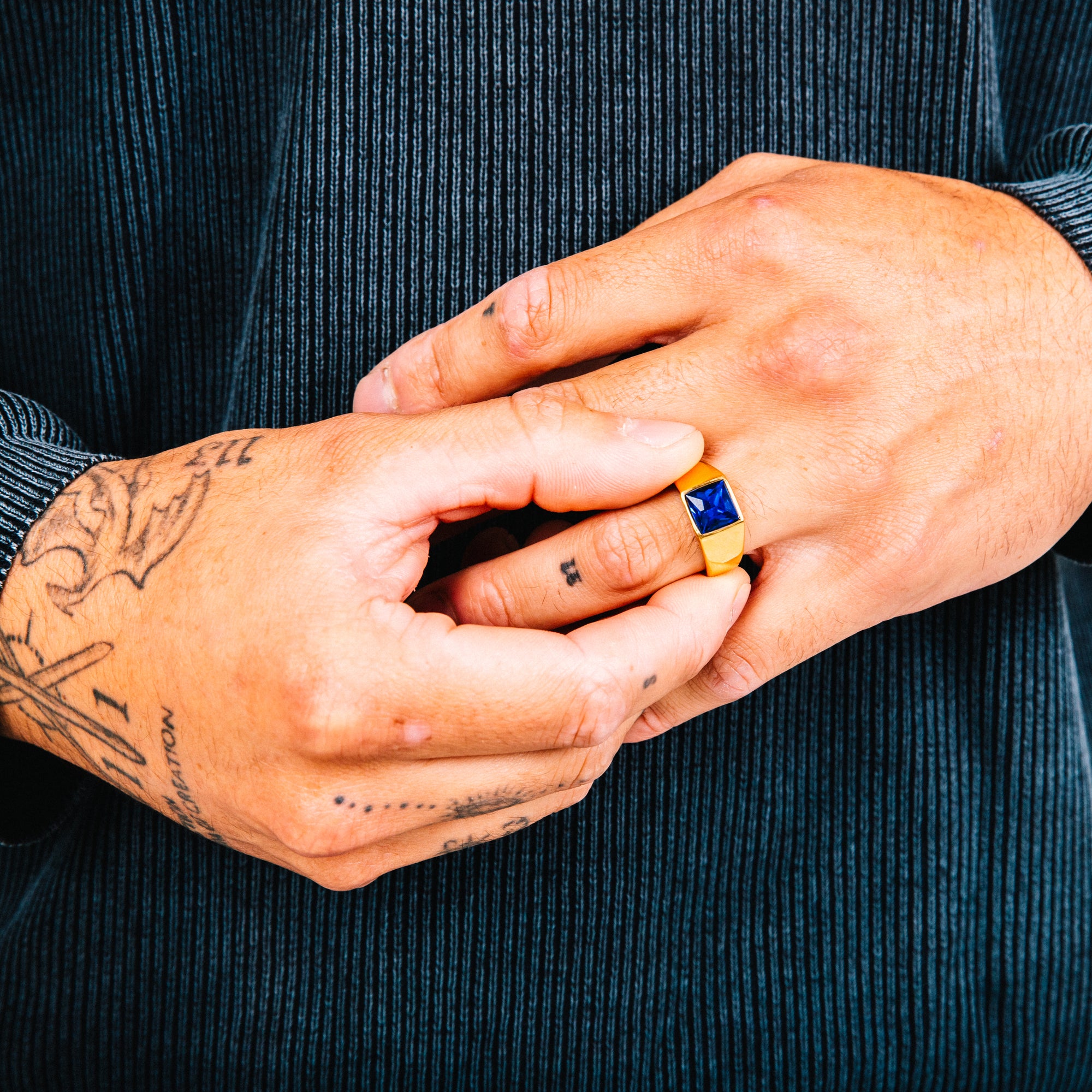 Close-up of hands with a ring featuring a blue gemstone against a dark background
