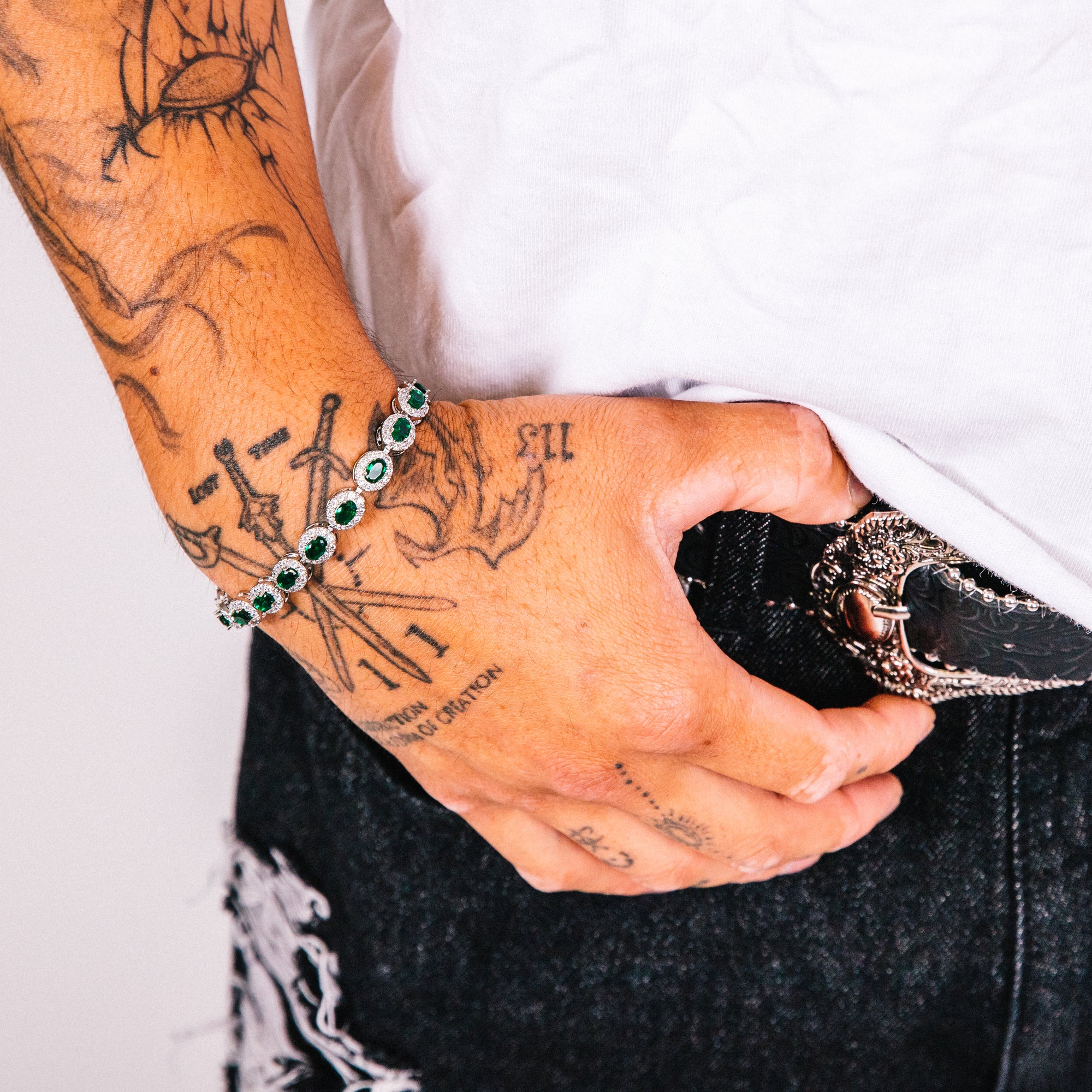 Person with tattoos wearing a bracelet and holding a phone with a white background