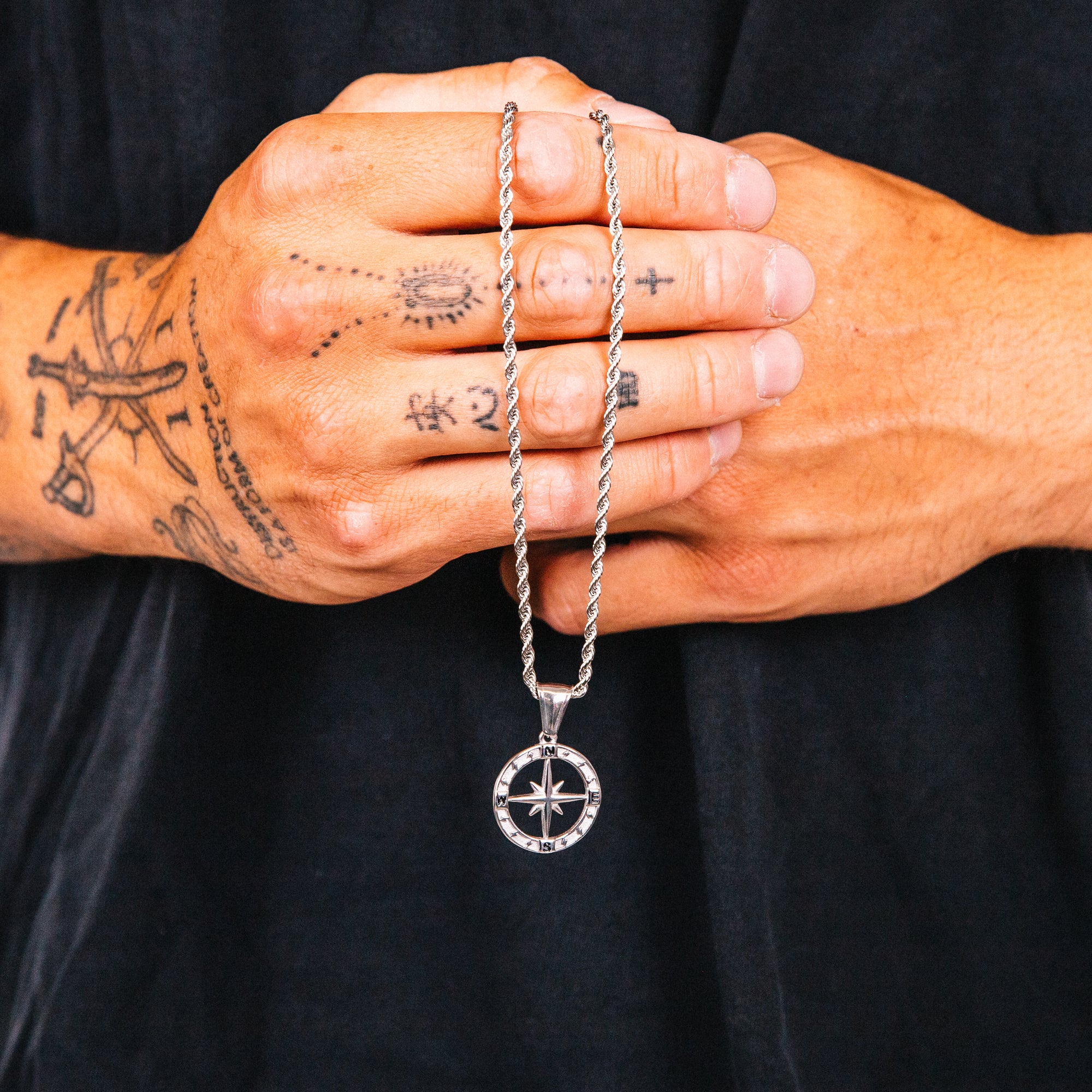 Person holding a silver necklace with a compass pendant against a black background