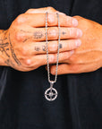 Person holding a silver necklace with a compass pendant against a black background